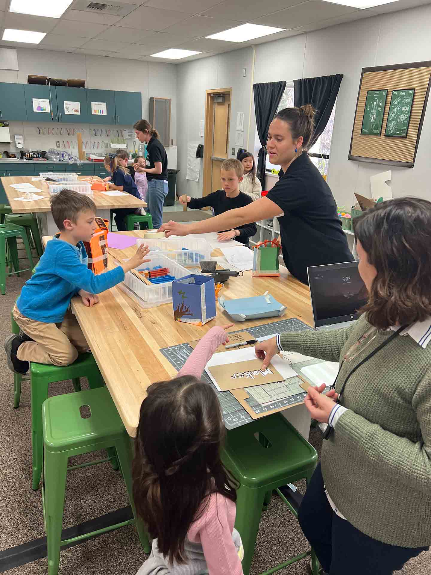 Two Cal Poly students at two separate tables help young children complete crafts in a classroom. 