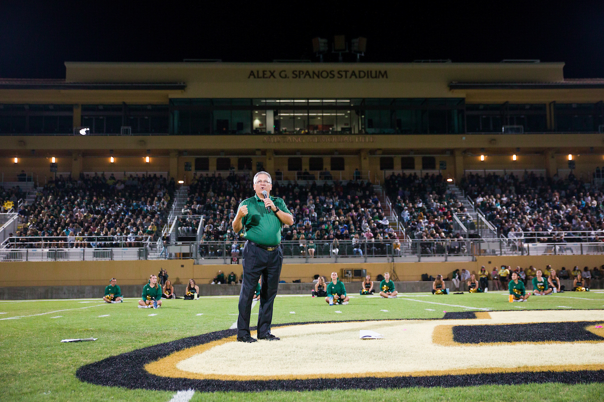 President Armstrong stands in the middle of the field at Spanos Stadium addressing first-year students as a torn sheet of paper falls to the ground on either side of him
