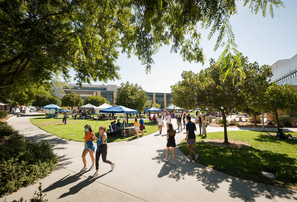 Groups of students walk around rows of booths and tents set up on the Engineering Plaza lawn