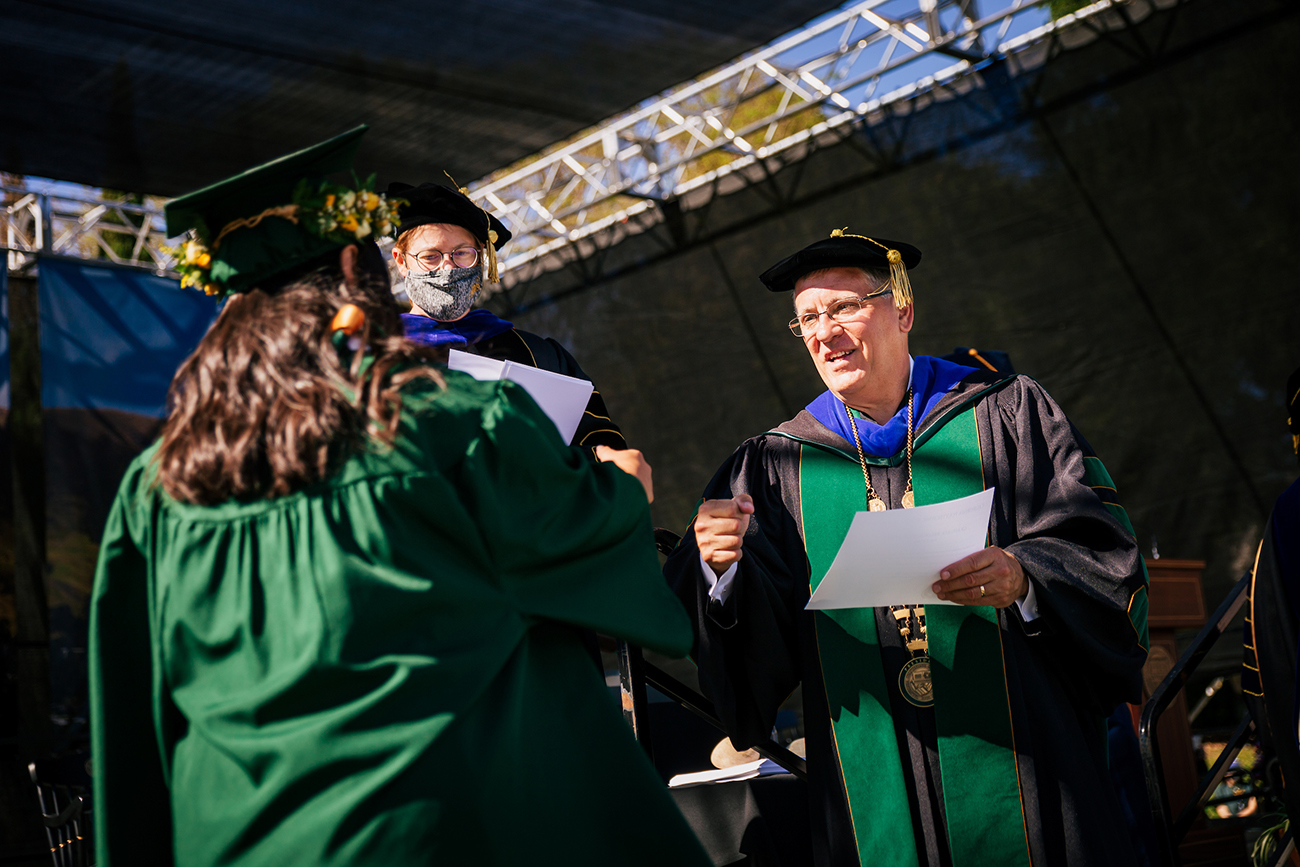 A student in a commencement gown shakes hands with president Jeffrey Armstrong, in academic regalia