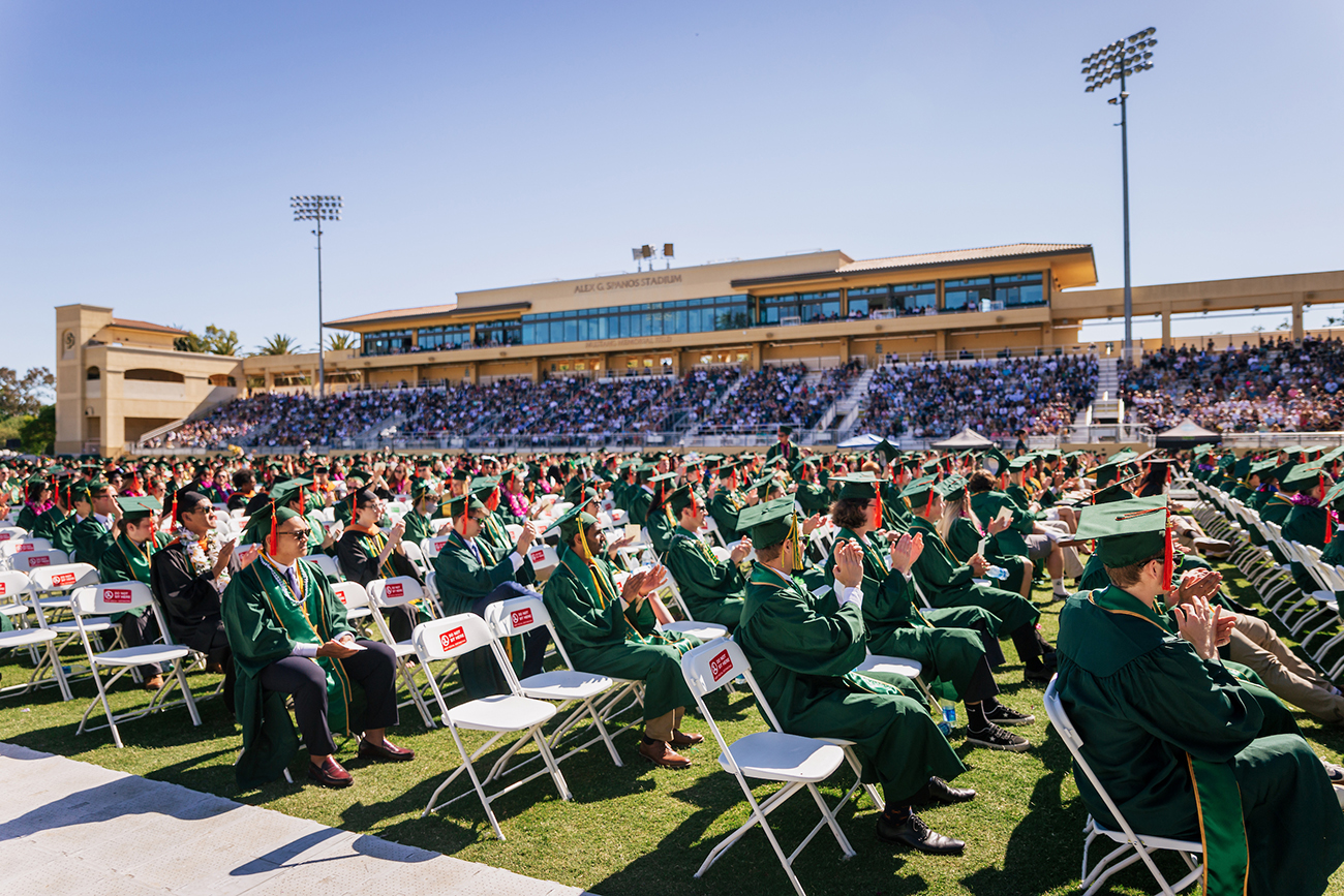 A crowd of graduates fills the field at Spanos Stadium, while thousands of friends and family watch from the stands.