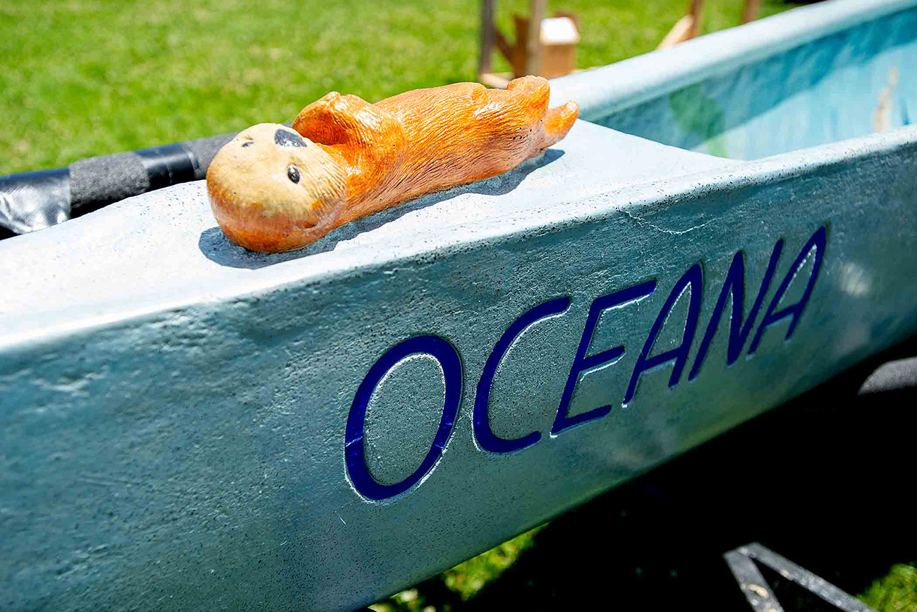 A small tan-and-yellow figure of an otter decorates the prow of a light blue canoe