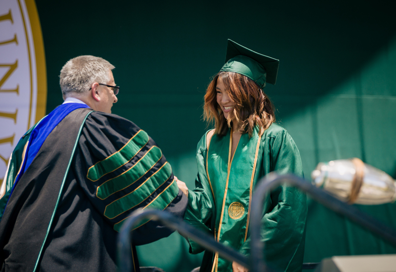 A student in a commencement gown shakes hands with president Jeffrey Armstrong, in academic regalia
