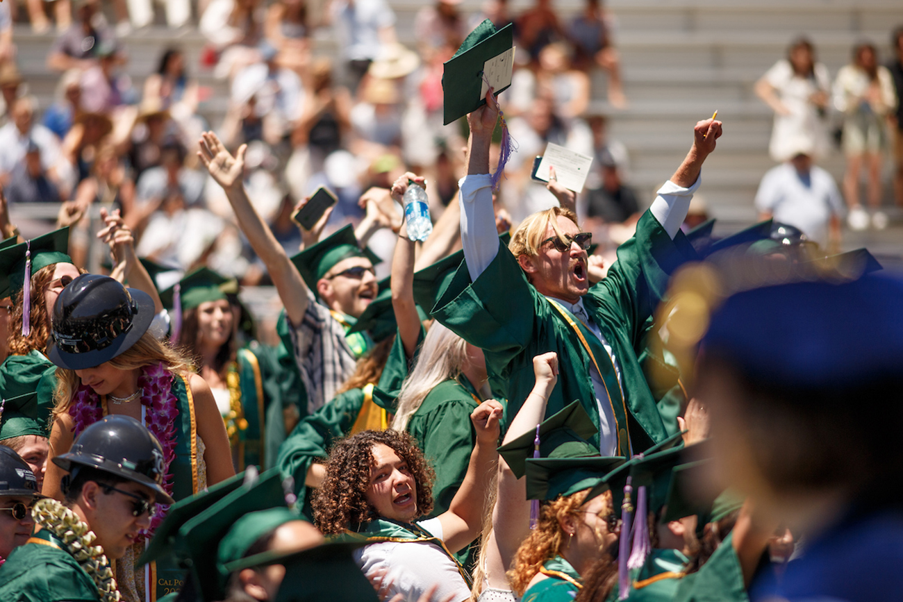 A group of graduates stands and cheers in Spanos Stadium.