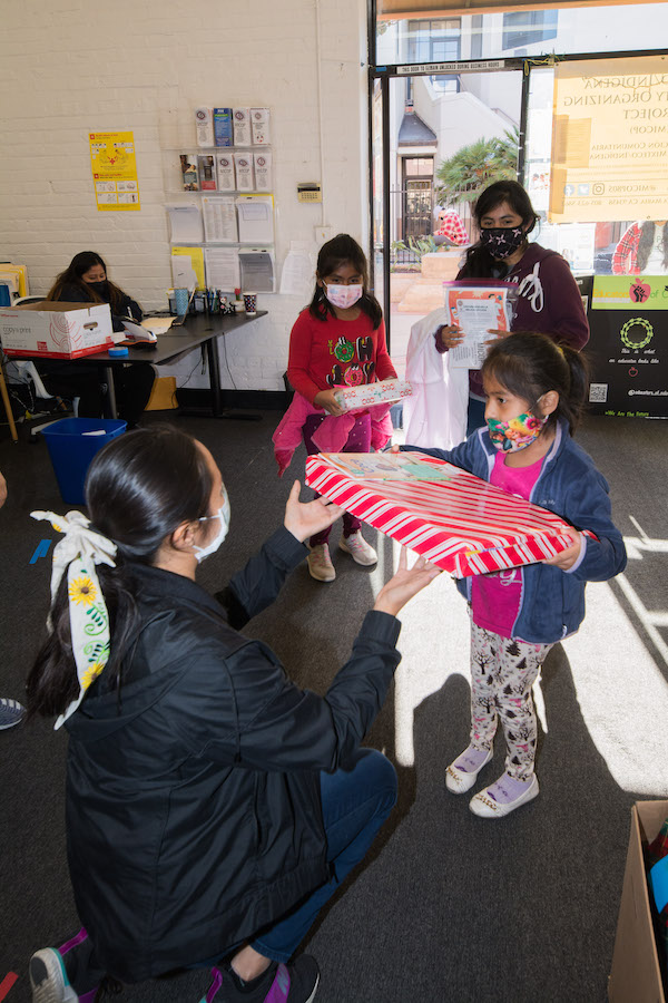 A student member of the Educators of Color club gives a gift to a young girl during a holiday book and gift drive.
