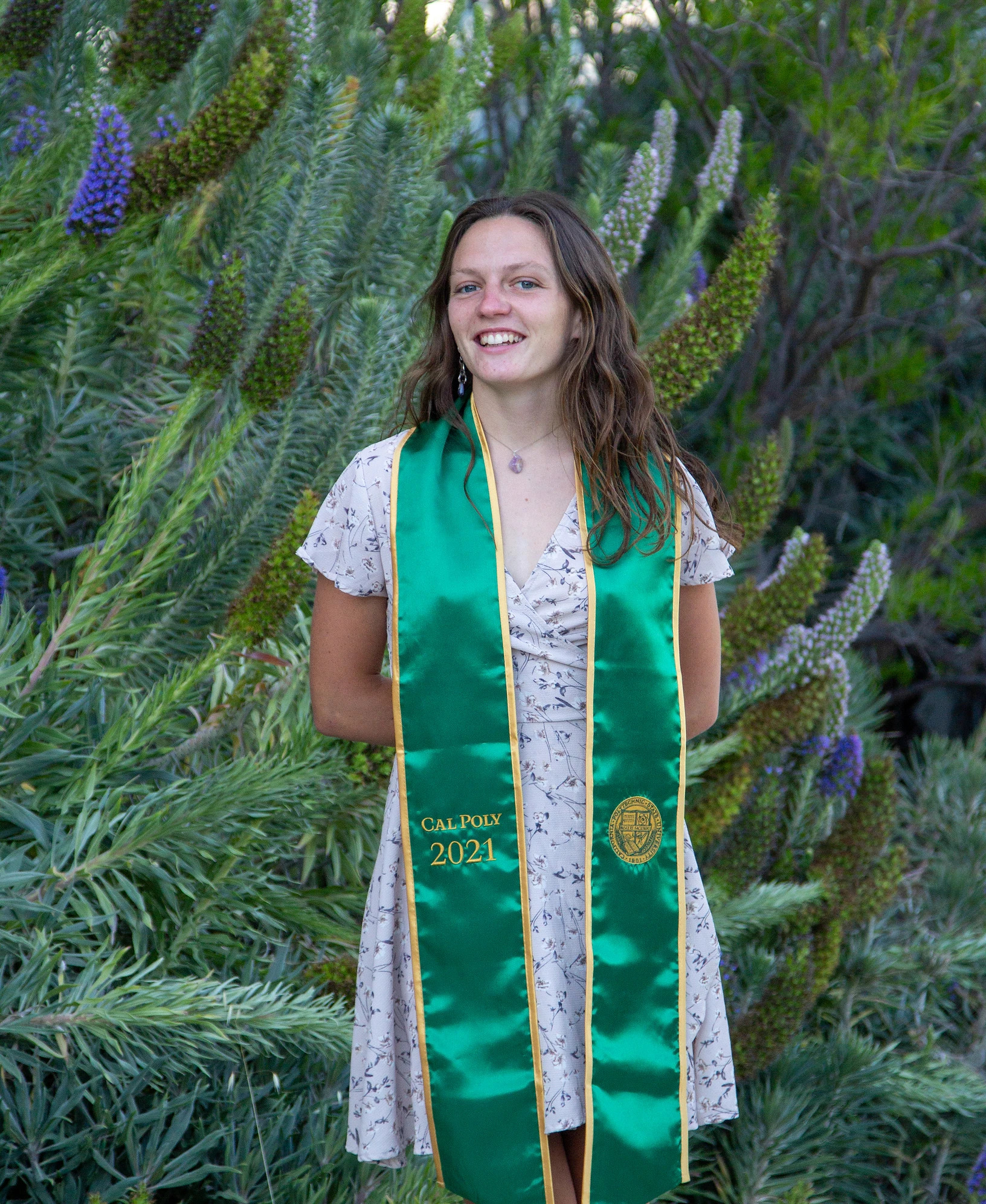 Noel Clark poses in a printed dress and a green Cal Poly graduation stole.
