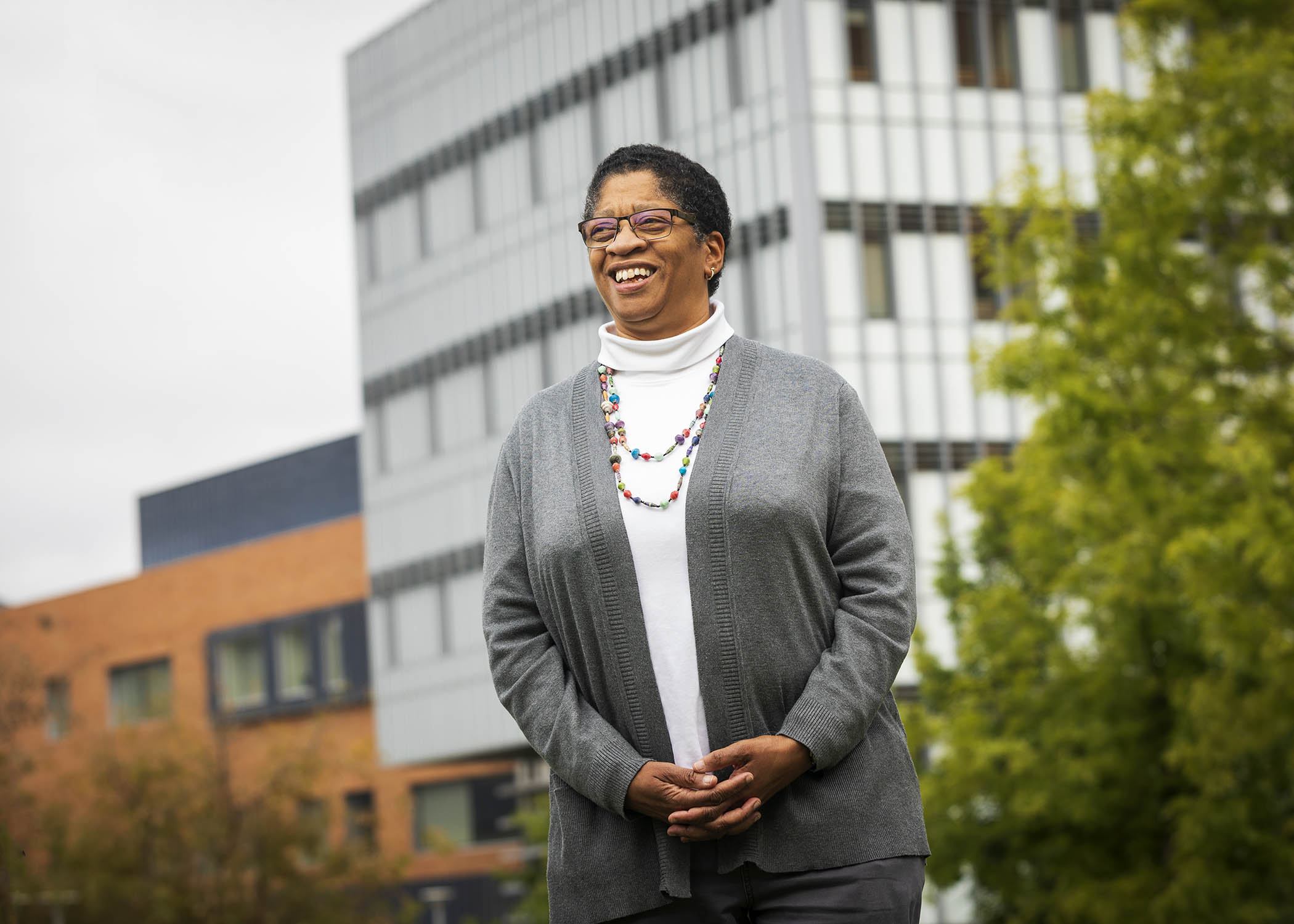 Kinesiology professor Camille O'Bryant smiles for a professional portrait outside on campus. She is wearing a white shirt and a gray cardigan.