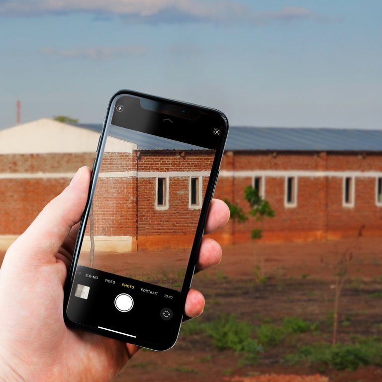 A phone is held up in front of a brick school building. The screen of the phone shows part of the building.