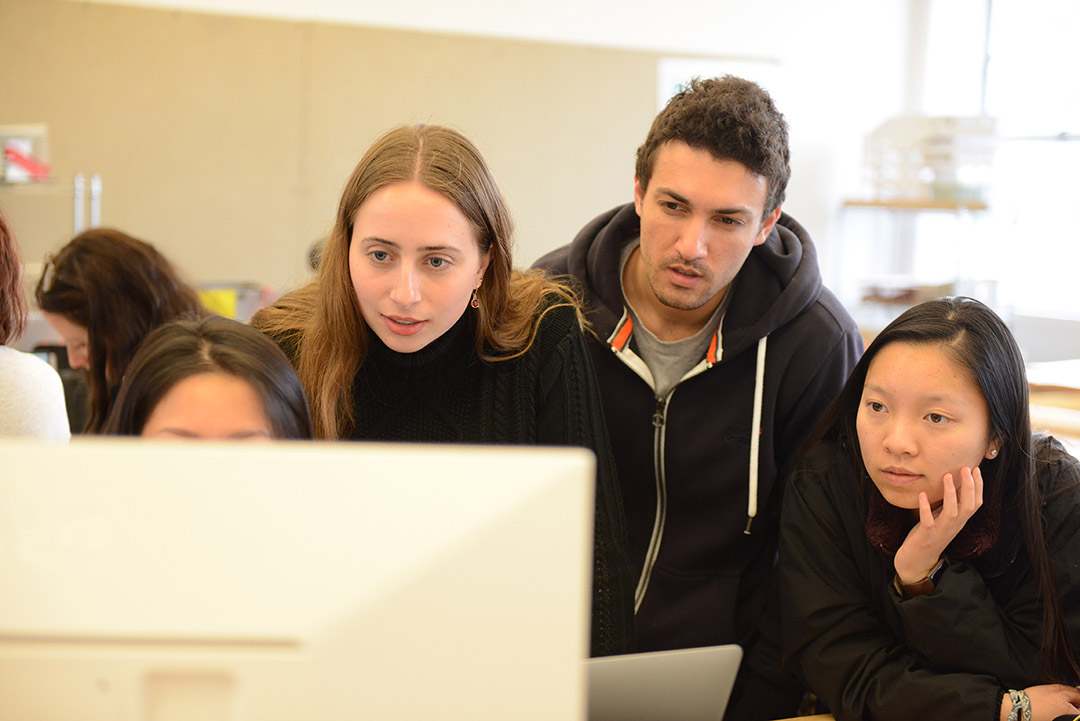 Three students look intently at something on a computer. 