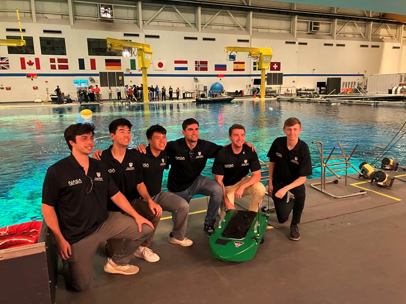 Six engineering students who worked on the SAVER autonomous device pose for a picture with their product in front of a swimming pool at NASA.