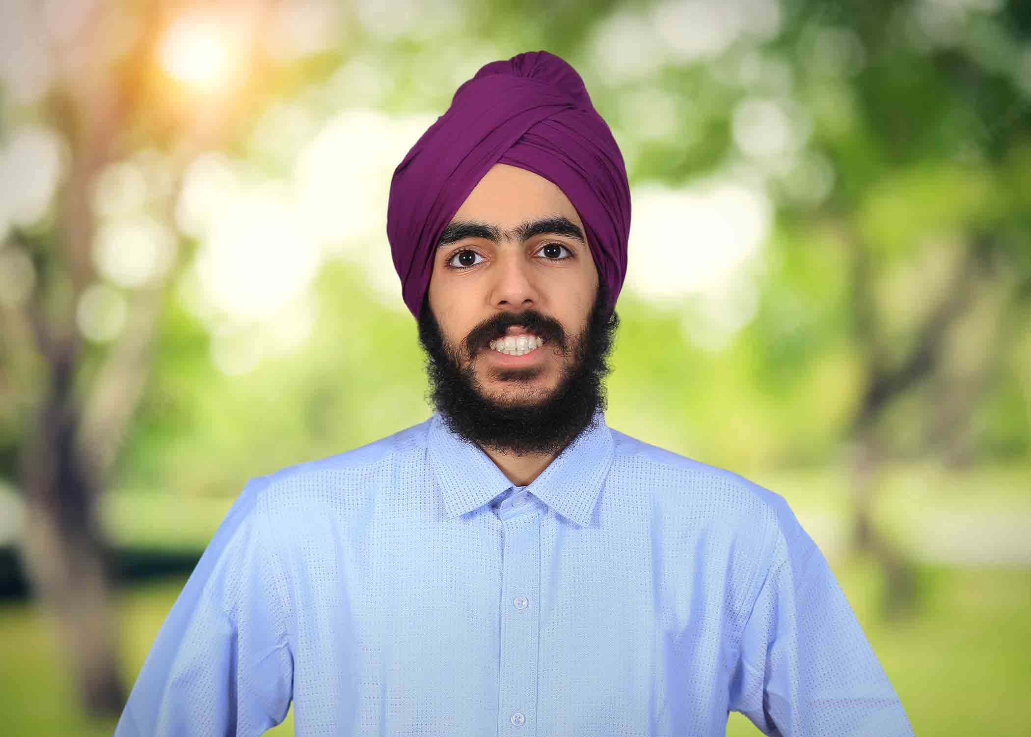 Karan Singh wears a blue button-down shirt and a magenta turban as he smiles for his headshot.