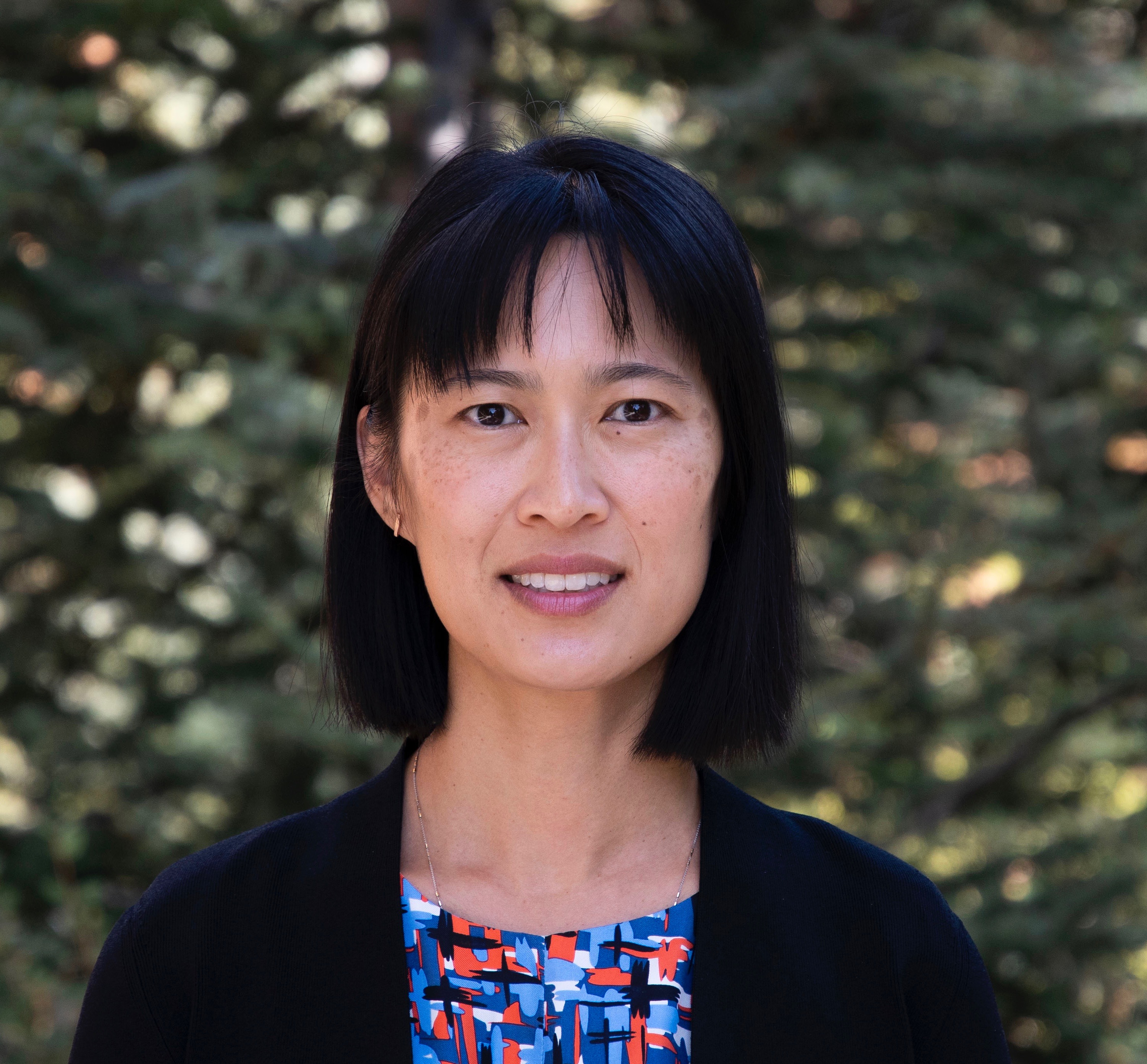 A headshot of professor Tina Cheuk wearing a printed blouse and black cardigan.
