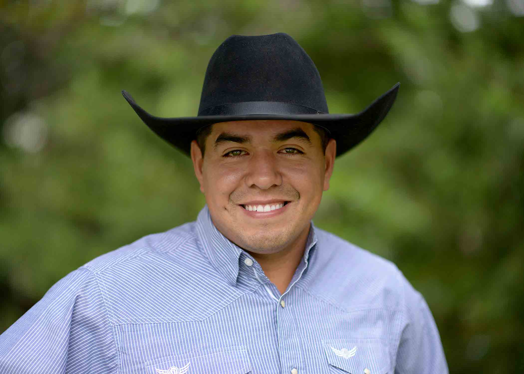 Rafael Velazquez-Ramos smiles in a black cowboy hat and blue button up shirt smiles.