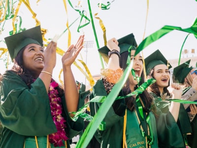 Three joyful students in graduation attire with confetti mid-air
