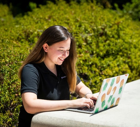 A student works outdoors at a laptop