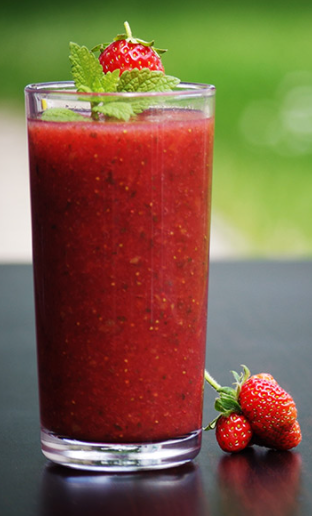 Strawberry smoothie in a glass with strawberries next to it. 