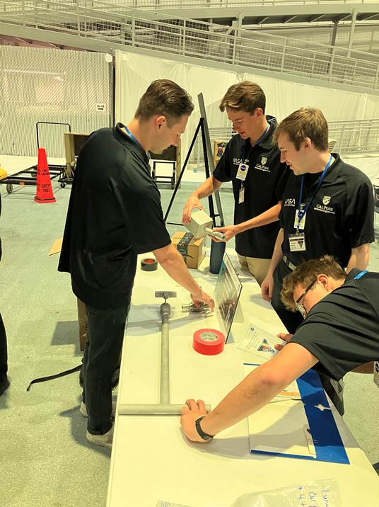 Four students gather around a protoype for an extension handle mechanism at NASA.