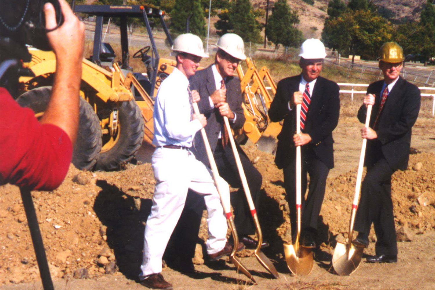 Four people in hard hats hold gold shovels at a groundbreaking on Cal Poly's campus