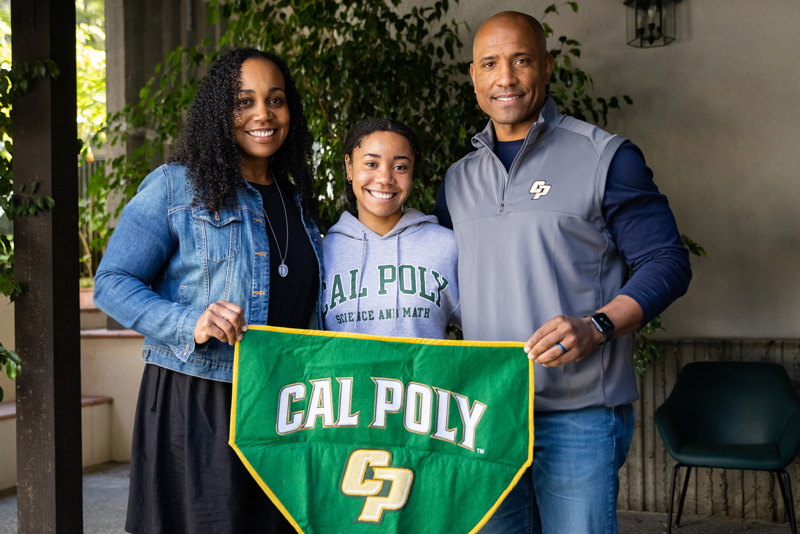 Dionna, Genesis and Victor Glover smile holding a green Cal Poly banner