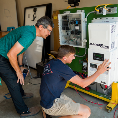 A professor and a student look at an inverter connected to solar panels in a lab