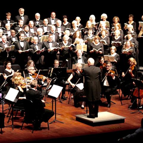 Conductor waves baton as the performers surround him on stage