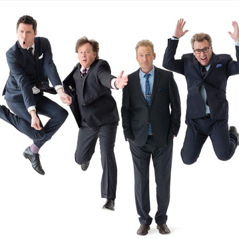 Four men in suits, jumping and standing while pointing at the camera