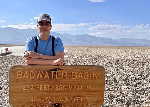 David Bains rests arm atop Badwater Basin sign in Death Valley National Park