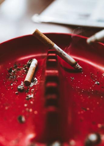 A red ashtray containing extinguished and smoldering cigarettes