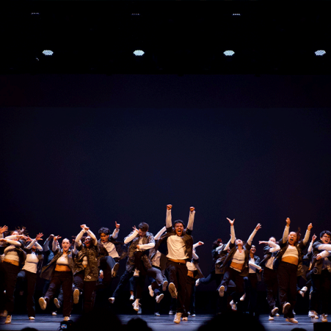 A line of United Movement dancers raise arms at the conclusion of a dance number on stage