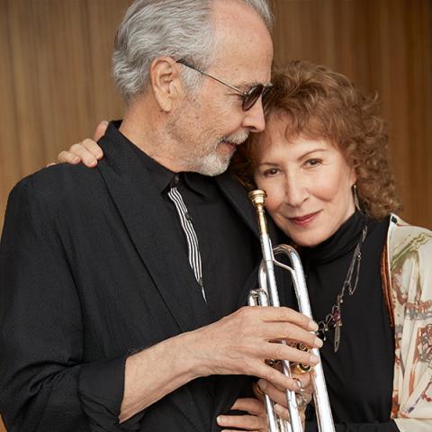 Herb Alpert and Lani Hall lean into each other-the man holding a trumpet