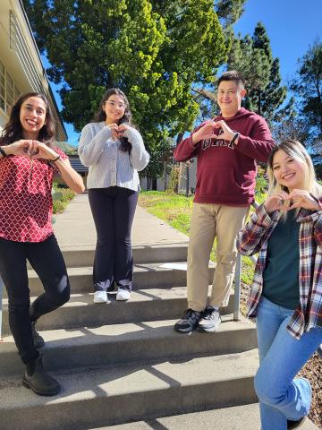 four people stand on steps making hearts signs with their hands