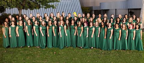 The Cantabile choir wearing green formal dresses assembles on the grass outside the Performing Arts Center