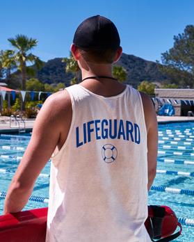 Image of a male wearing a Lifeguard tanktop while holding a lifeguard float while looking at a lap swimming pool