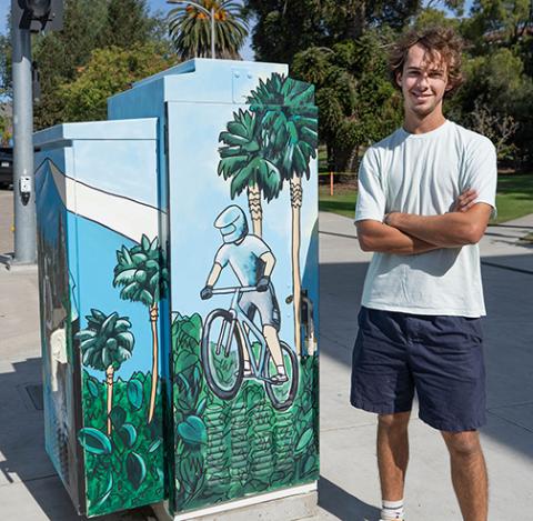 Chet Crummett stands next to the mural he painted on a Cal Poly utility box