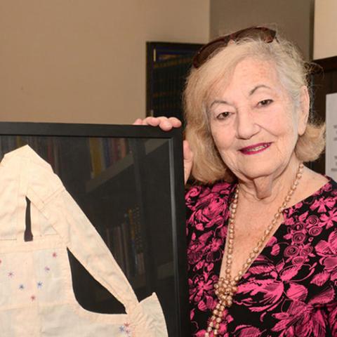 Holocaust survivor Goldie Jacoby holds her childhood apron that is in a frame behind glass