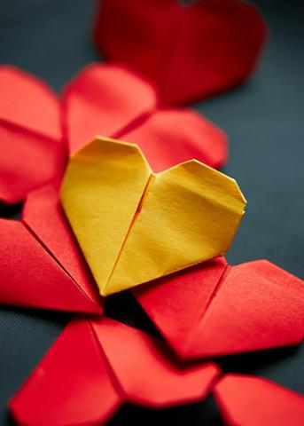 A series of seven folded paper red hearts topped by a yellow paper heart