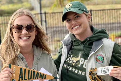 A pair of alumae holding Cal Poly pennants 