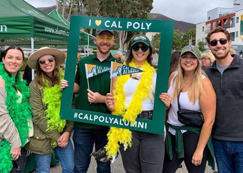 A group of six men and women Cal Poly alumni pose with an alumni frame