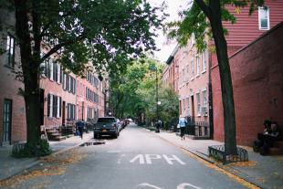Tall brick apartment buildings line a narrow city street