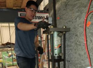 Graduate student researcher Jerry Luong makes final adjustments to the axial load system before testing a concrete wall in 2019
