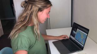 A young woman in a green shirt works on a laptop displaying satellite orbital trajectories