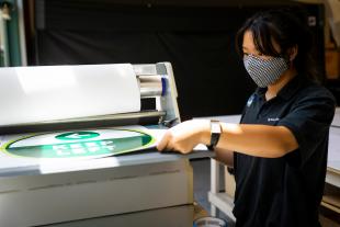 Michaela Kwan laminates a newly printed sign as she and other student employees print signage to be used in buildings on campus during the coronavirus pandemic. 