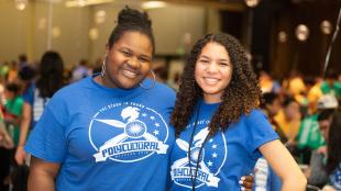 Two people in blue PolyCultural Weekend event shirts smile at the 2019 event at Cal Poly