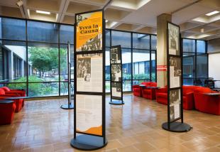 A cardboard poster exhibit that says ¡Viva La Causa! in black letters over an orange and gray background is part of several poster exhibits in one of the main areas of Kennedy Library.