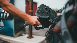 A hand inserts a gasoline pump nozzle into the fuel hatch of a black car