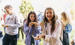 Two female students smile in surprise as they hold lime and lemon wedges during a taste test party on campus.