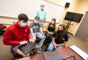 A group of five Cal Poly students wearing face masks gather around a computer as they collaborate on this 