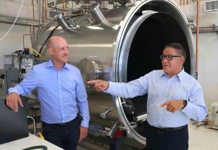An aerospace engineering lecturer and Congressman Salud Carbajal chat in front of a new piece of equipment at the Advanced Technologies Lab.