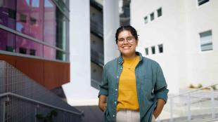 Student Nathalie Zamora, in a denim shirt and yellow tee, smiles in a portrait on campus.