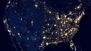 An aerial view of the United States at night with major cities illuminated with light